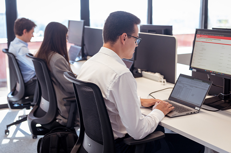 três jovens sentados em secretárias a trabalharem em computadores portáteis